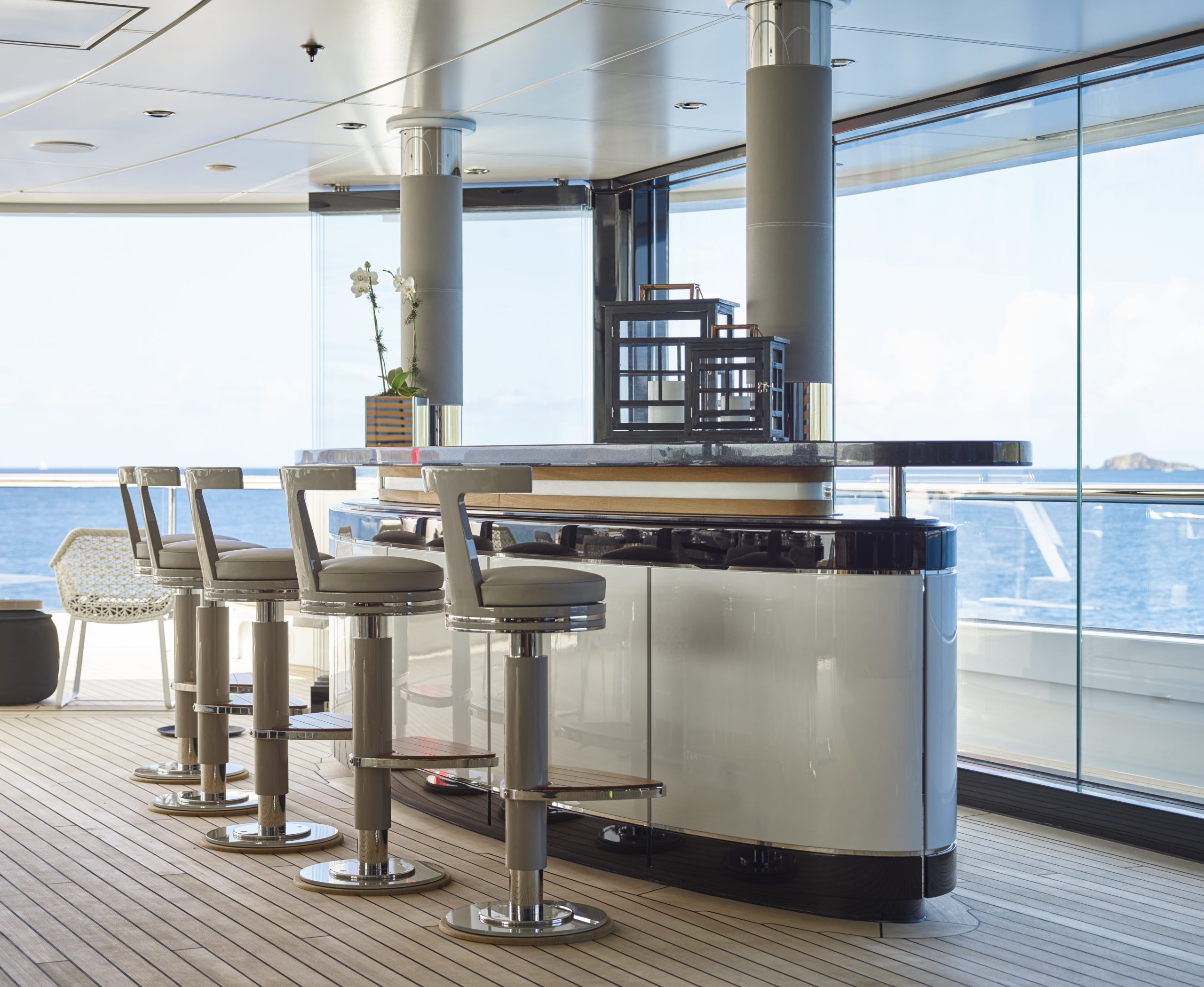 Moderne Bar mit hellen Barhockern und Glasreling auf dem hölzernen Außendeck einer Yacht