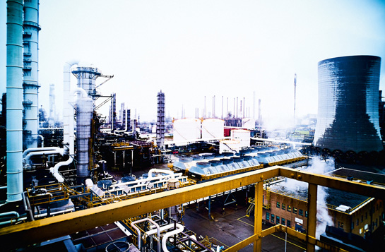 Panorama einer weitläufigen Industrieanlage mit Kühlturm, Schornsteinen und komplexen Rohrleitungssystemen