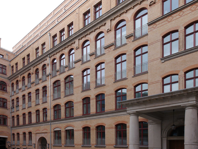 Außenansicht eines mehrstöckigen, sanierten Backsteingebäudes mit Rundbogenfenstern und klassischen Zierelementen