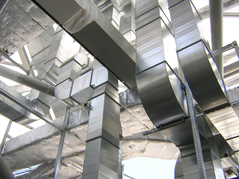 Komplexe Anordnung von rechteckigen, verzinkten Blechkanälen und isolierten Rohrleitungen in einem modernen Industriegebäude