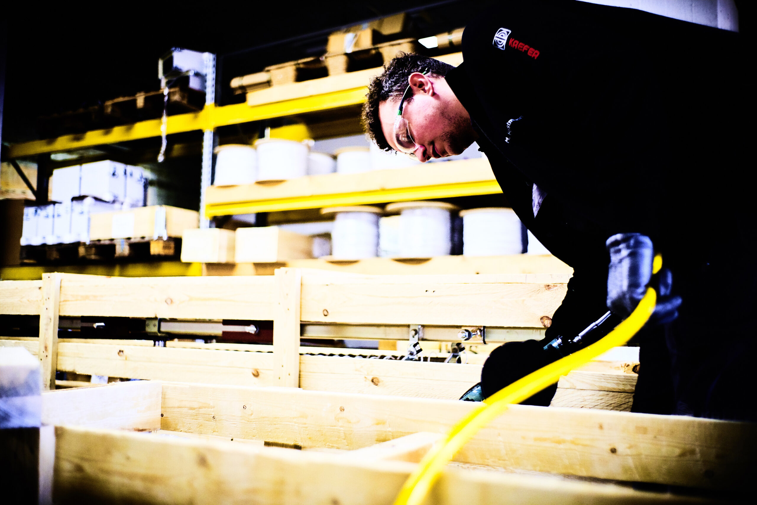 Ein KAEFER Mitarbeiter mit Schutzbrille, der an Holzplatten arbeitet