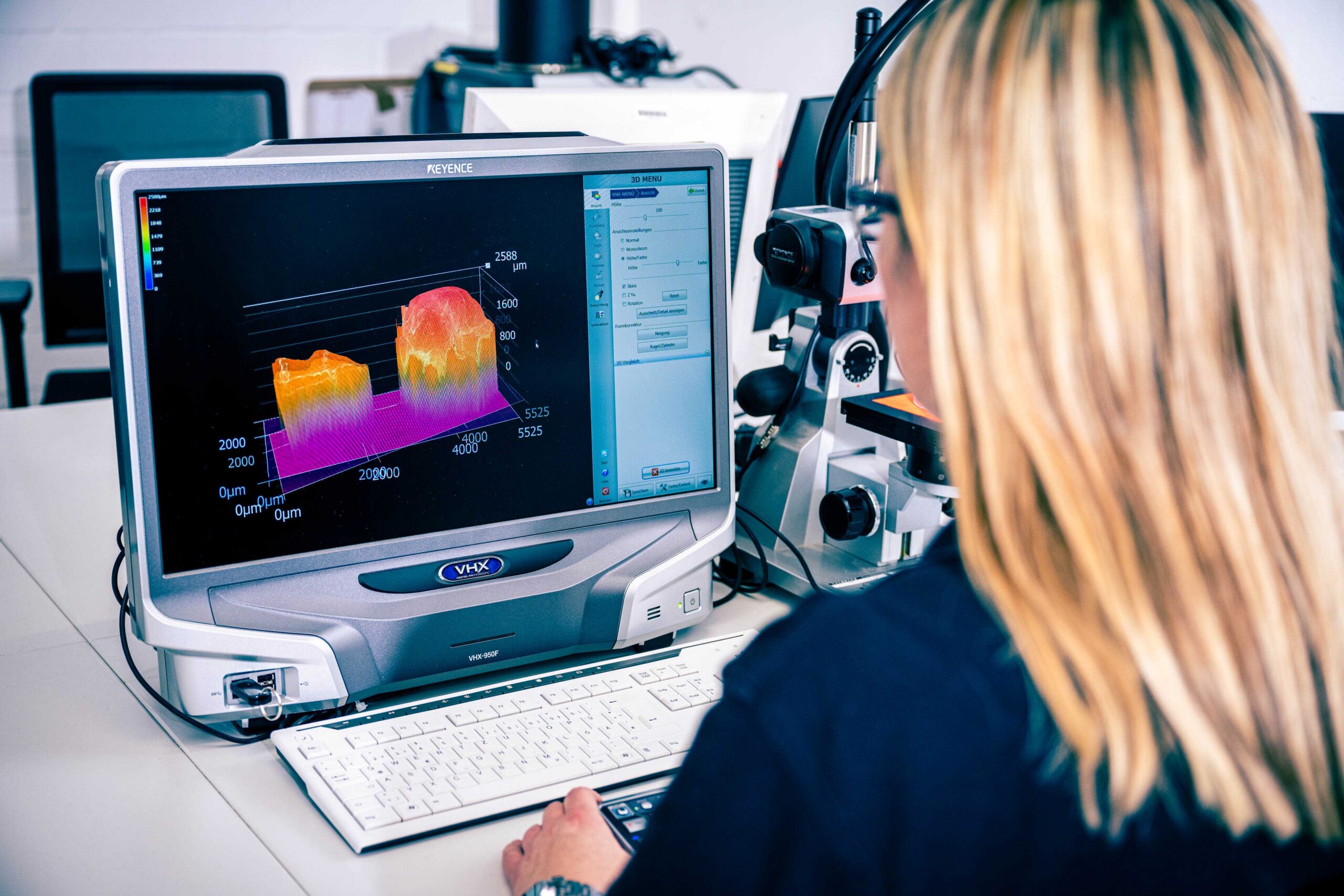 Eine KAEFER Mitarbeiterin analysiert am Monitor eines Digitalmikroskops die farbige 3D-Oberflächentopografie einer Materialprobe