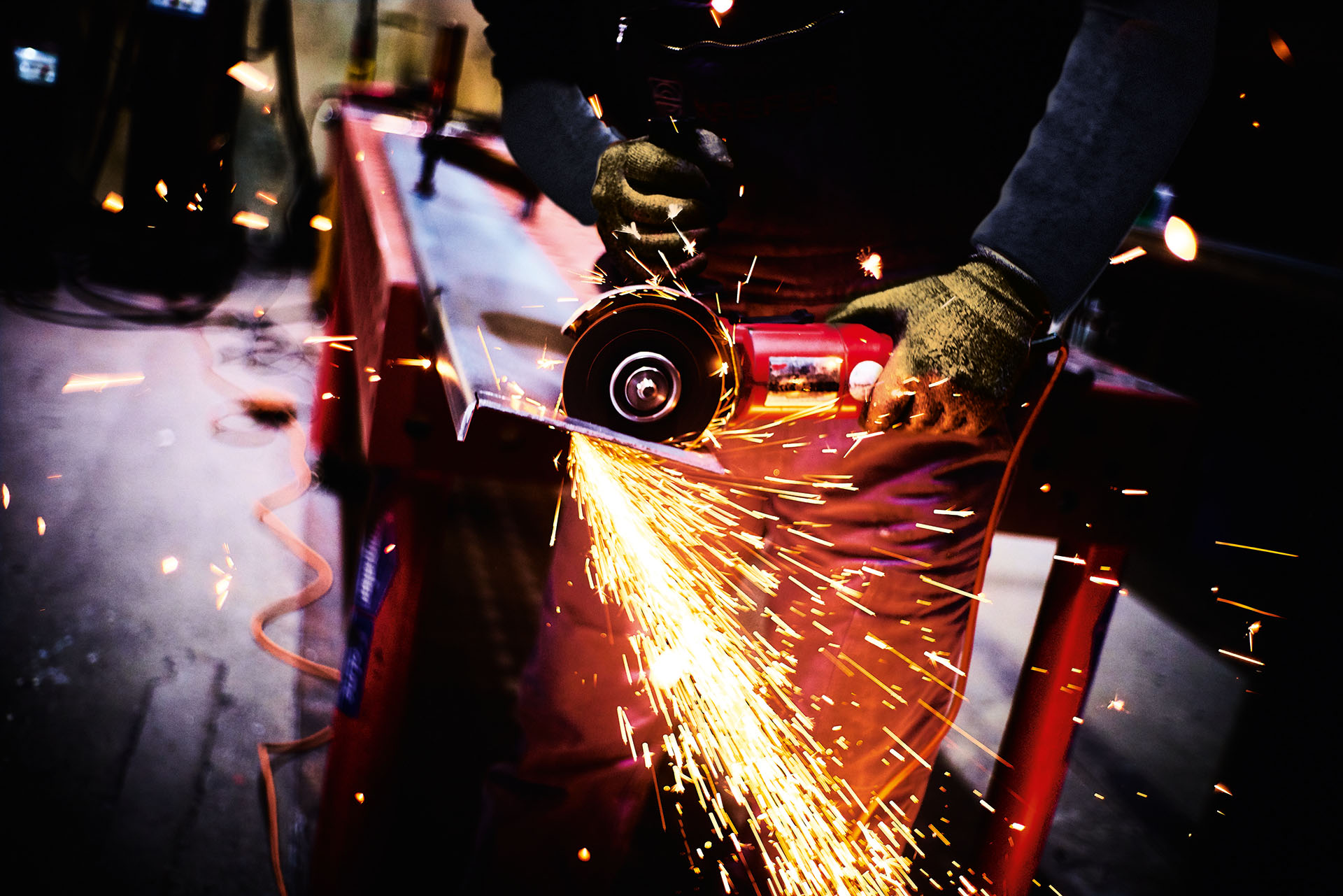 Detailaufnahme einer Metallbearbeitung mit einem Winkelschleifer, bei der ein intensiver Funkenflug beim Zerspanen einer Stahlkante entsteht
