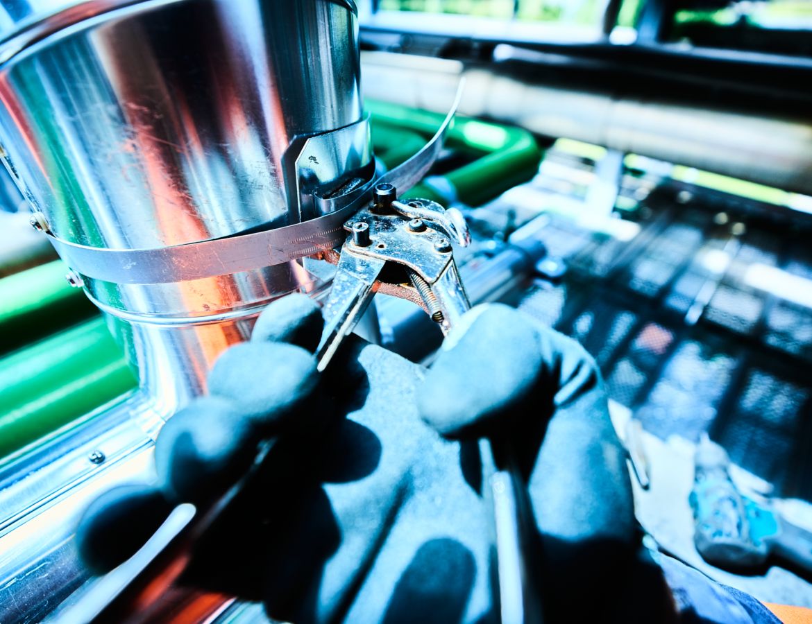 Nahaufnahme einer Hand mit Schutzhandschuh, die mit einer Zange an einem rohr arbeitet