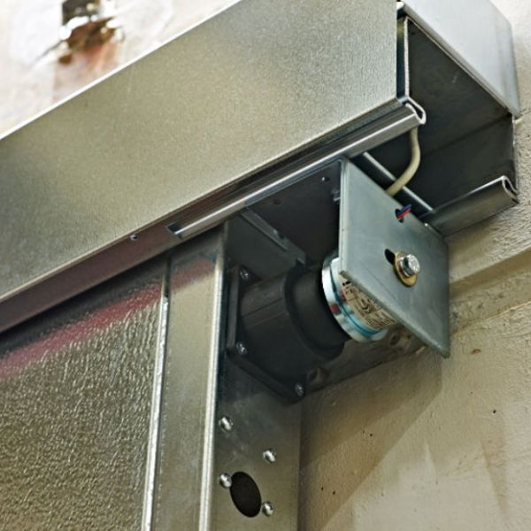 Nahaufnahme einer technischen Brandschutz-Vorrichtung mit metallischer Laufschiene und einem elektromechanischen Feststellmechanismus an einer Wand