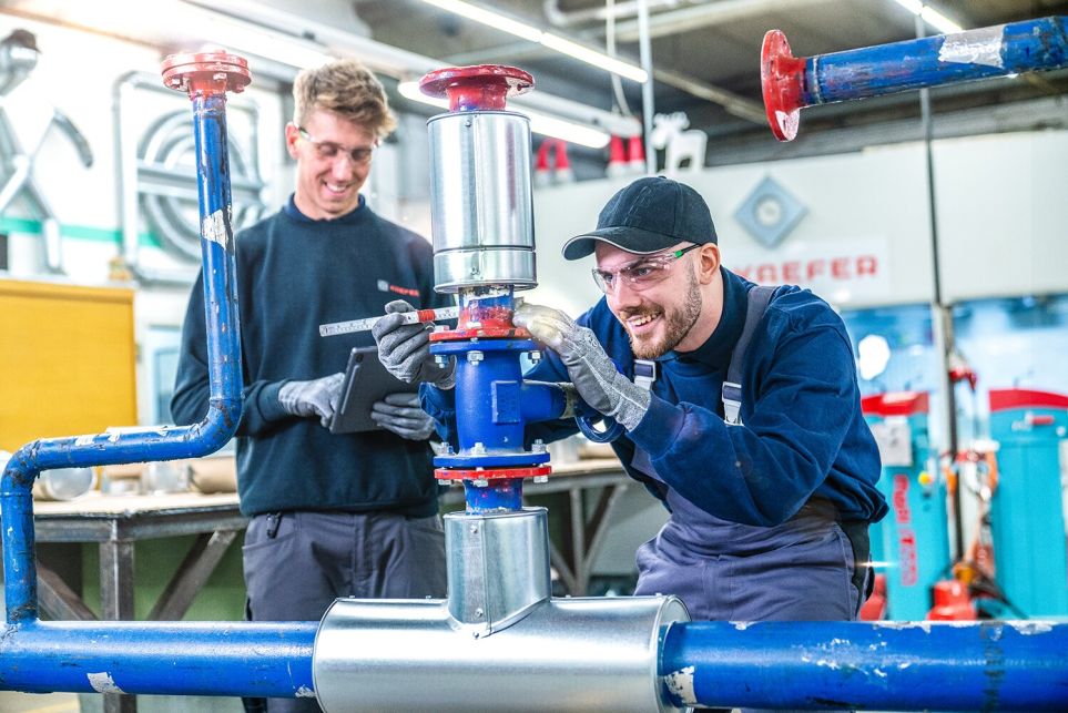 Zwei Männer arbeiten an einer Rohrkonstruktion in einer Werkstatt