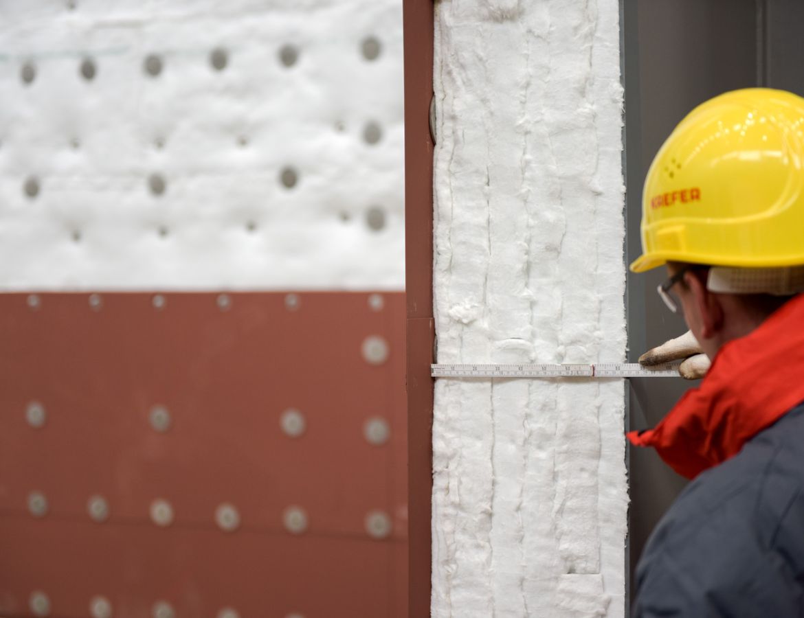 Ein KAEFER Mitarbeiter misst die Dicke einer Dämmschicht an einer Wandkonstruktion
