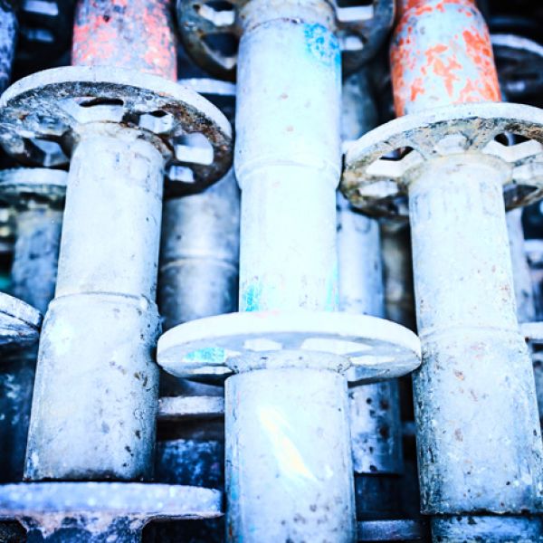 Nahaufnahme von vertikal gelagerten, gebrauchten Gerüststielen aus verzinktem Stahl mit typischen Lochscheiben-Anschlüssen