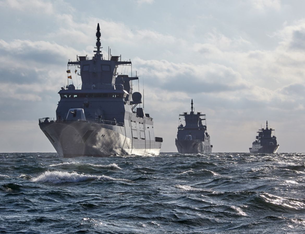 Three naval vessels sailing in a line on the open sea