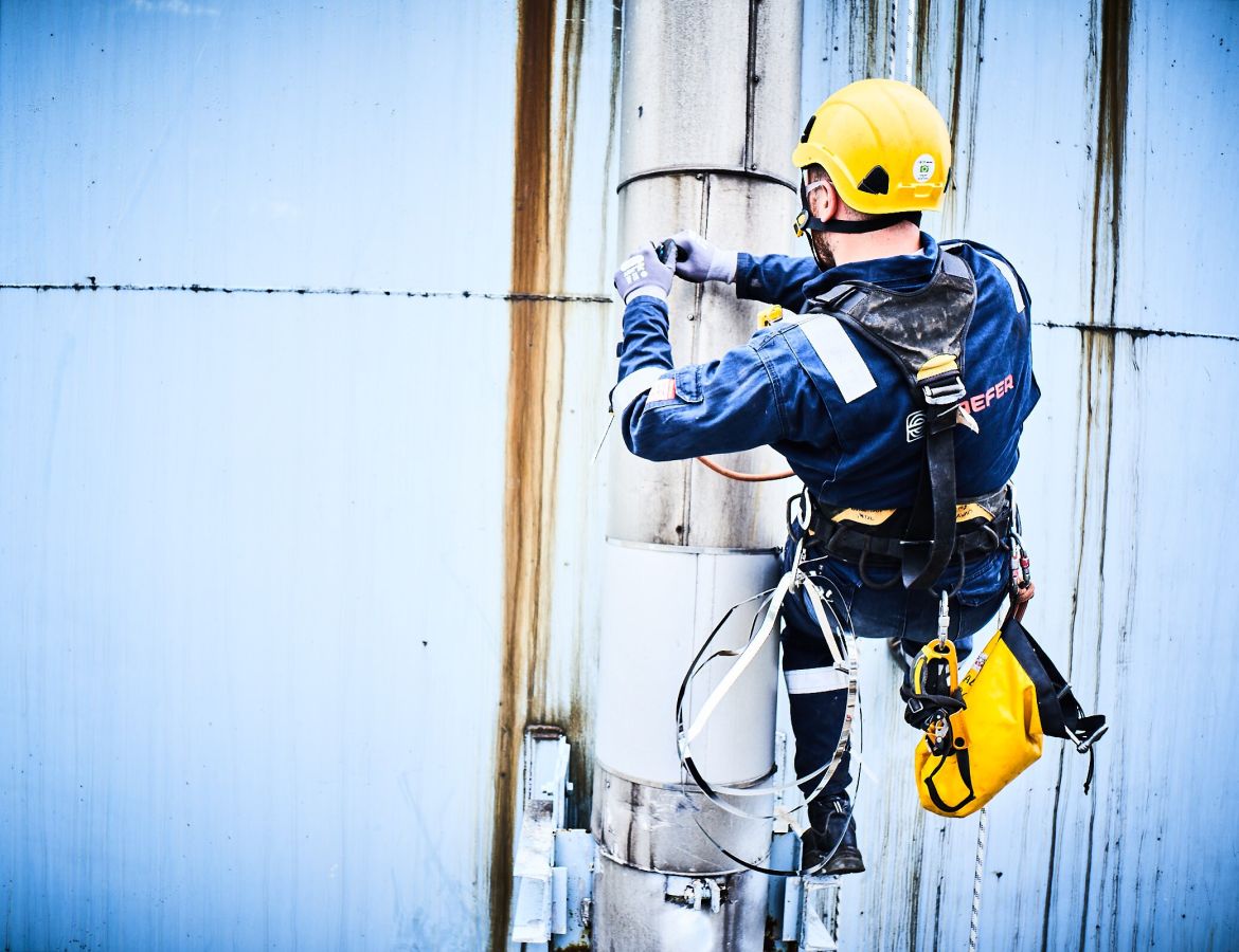 Ein KAEFER Kletterer hängt an einem Sicherheitsgurt und arbeitet an einem Rohr an der Außenwand eines Silos