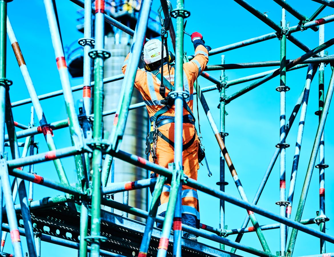 Ein gesicherter KAEFER Industriekletterer in voller Schutzausrüstung bei Montagearbeiten in schwindelerregender Höhe auf einem komplexen Gerüstbau