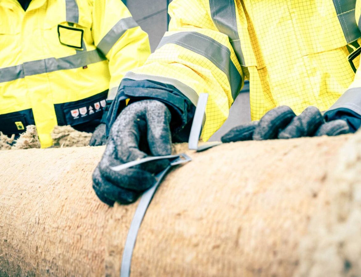 Nahaufnahme eines KAEFER Monteurs, der eine Mineralwolle-Rohrisolierung fachgerecht mit einem Metall-Spannband fixiert