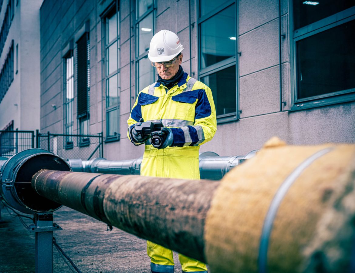 Ein KAEFER Mitarbeiter steht neben einem Rohr und scannt es mit einer Kamera