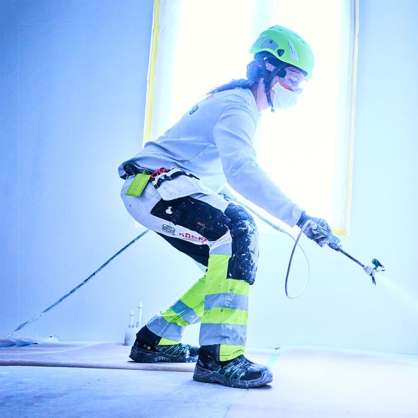 Frau in Malerkleidung beim Innenausbau und sprüht weiße Farbe an eine Wand
