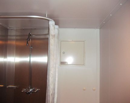 A shower with a shower curtain in one corner and a small rectangular door in the wall next to it