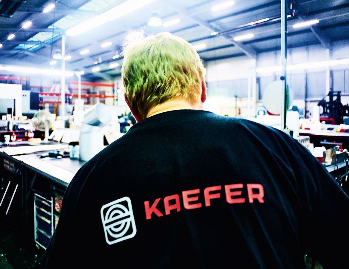 Rückansicht eines KAEFER Mitarbeiters mit KAEFER Logo auf der Kleidung, in einer Werkstatt